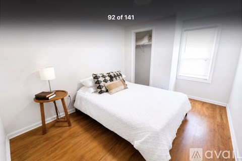 A bedroom with a bed, a small table with a lamp, and a window.
