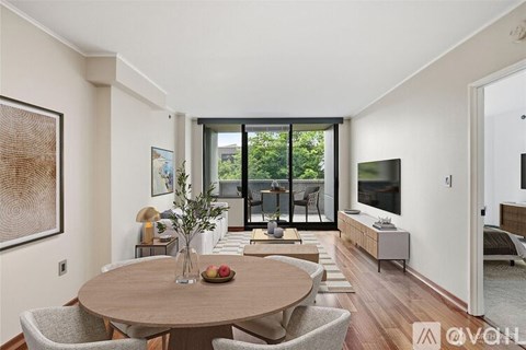 A modern dining room with a round wooden table and chairs, a vase with flowers, and a large window with a view of the outdoors.