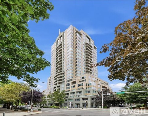 A tall residential building is surrounded by trees and has a clear blue sky above it.