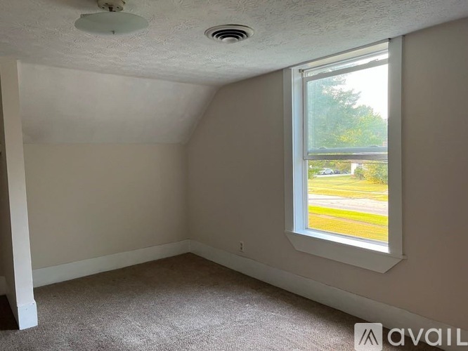 A room with a window showing a view of a parking lot and trees.