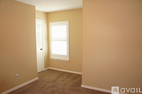 A room with a carpeted floor, a door, and a window with blinds.