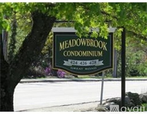 A sign for Meadowbrook Condominium stands in front of a tree.