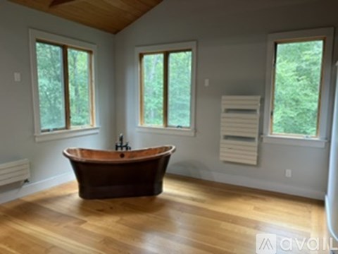 A wooden bathtub is in a large bathroom with a window.