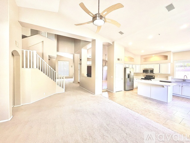 A spacious living room with a staircase and a kitchen area.