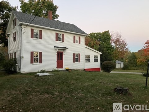A white house with red doors and windows sits in a grassy yard.