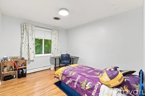 A bedroom with a bed covered in a purple blanket with a logo on it.
