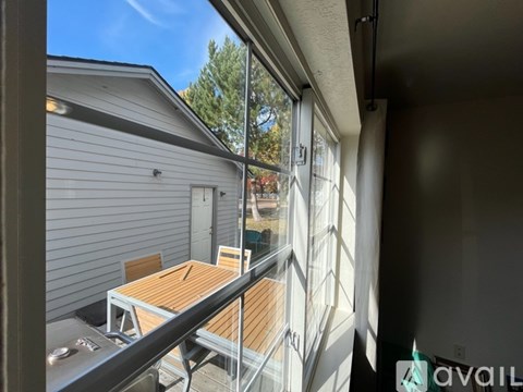 A balcony with a table and chairs overlooks a house and trees.