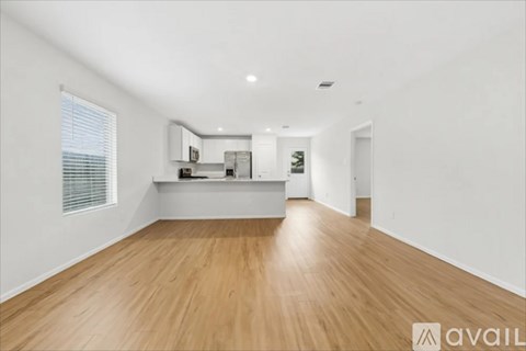 A spacious room with wooden flooring and a kitchen area in the background.