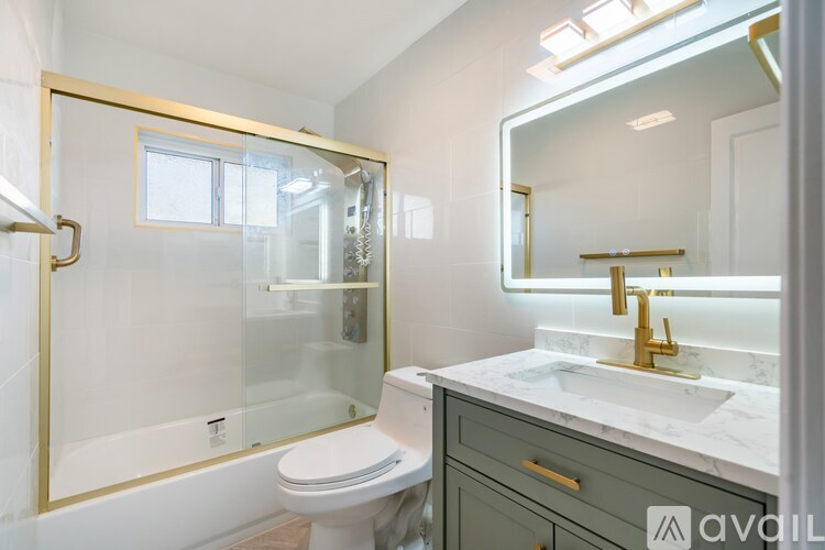 A bathroom with a white toilet, a sink with a gold faucet, and a gold framed mirror.
