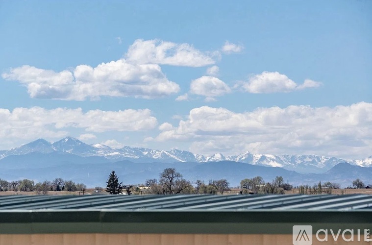 A mountain range with snow capped peaks in the distance behind a field with a tree and a building.