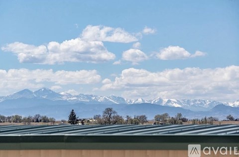 A mountain range with snow capped peaks in the distance behind a field with a tree and a building.