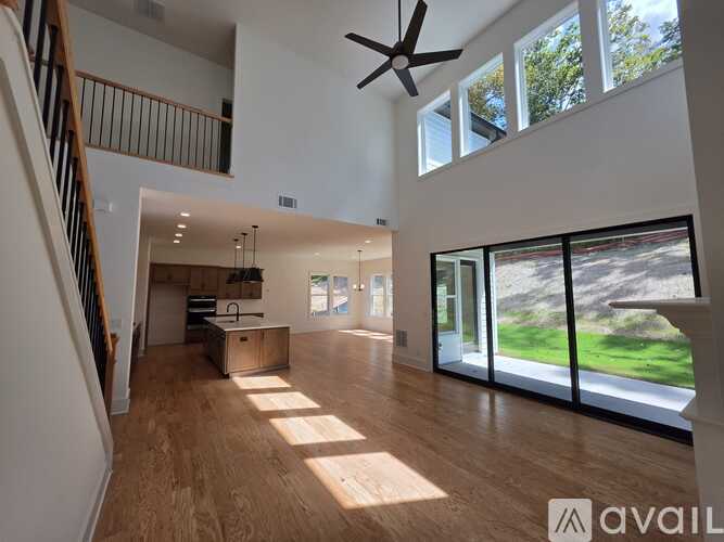 A spacious living room with a staircase on the left and a view of the outdoors through large windows on the right.
