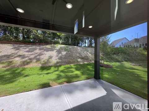 A covered patio area with a view of a grassy hill and trees.