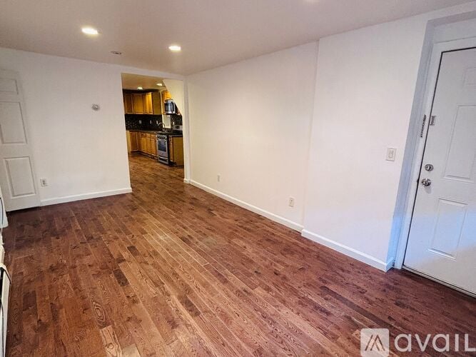 A room with wooden flooring and white walls, with a door on the right.