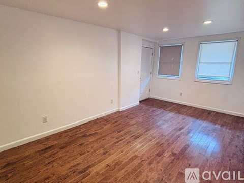 A room with wooden flooring and two windows.