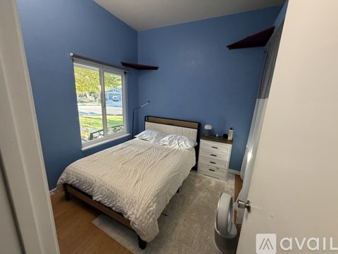 A bedroom with blue walls and a bed with a white comforter.