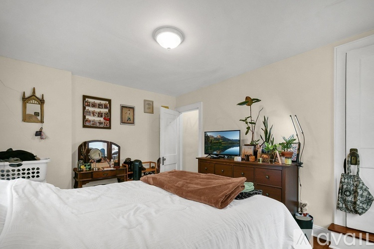 A bedroom with a white bed and a wooden dresser.