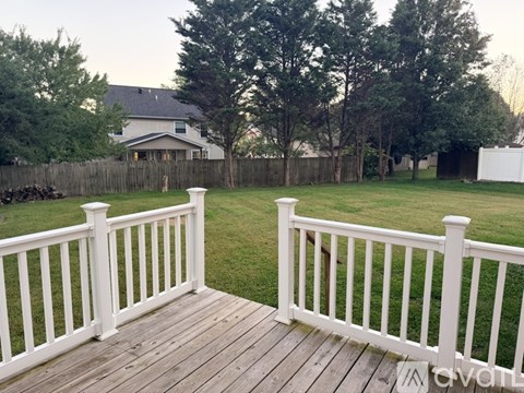 A wooden deck with a white railing leads to a backyard with a lawn and trees.