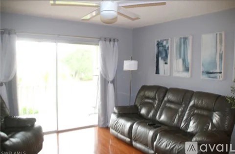 A black leather sofa sits in a living room with a ceiling fan and sliding glass doors.