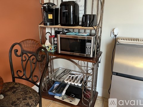 A kitchen with a microwave on a shelf and a chair.