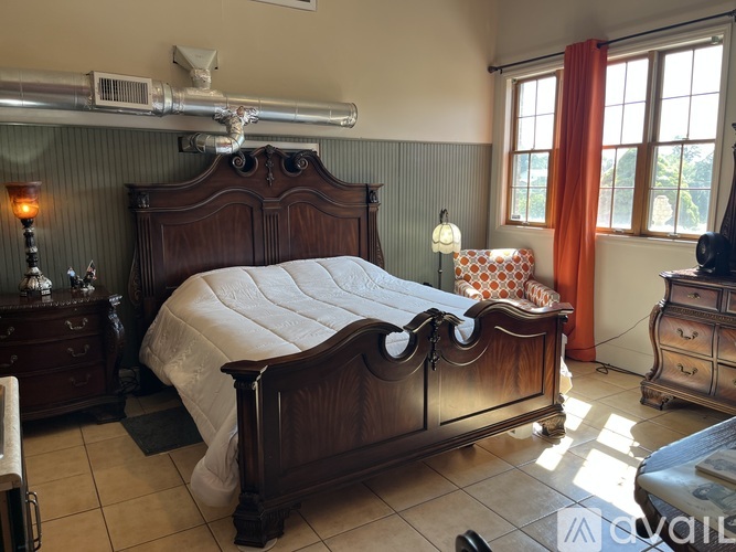 A bedroom with a large bed and a window with orange curtains.