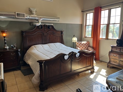 A bedroom with a large bed and a window with orange curtains.