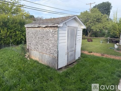 A shed with a damaged side is surrounded by green grass.