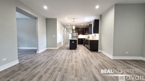 A spacious, empty room with wood flooring and a kitchen area in the background.