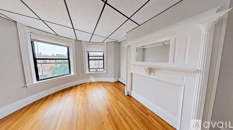A room with wooden floors and white walls, with a window showing a view of buildings and trees.