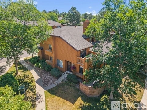 A house with a brown roof and a brown fence is surrounded by green trees.