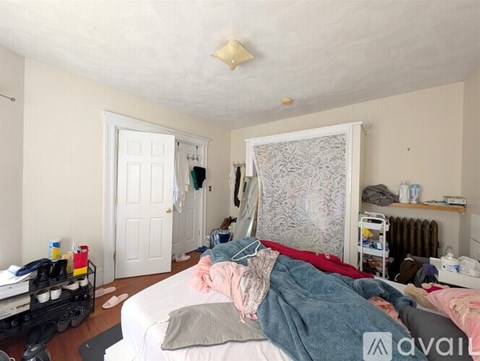 A messy bedroom with a bed in the center and a window with curtains to the right.