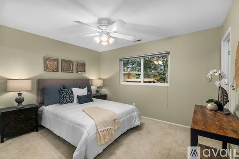 A bedroom with a bed, two lamps, a ceiling fan, and a window.