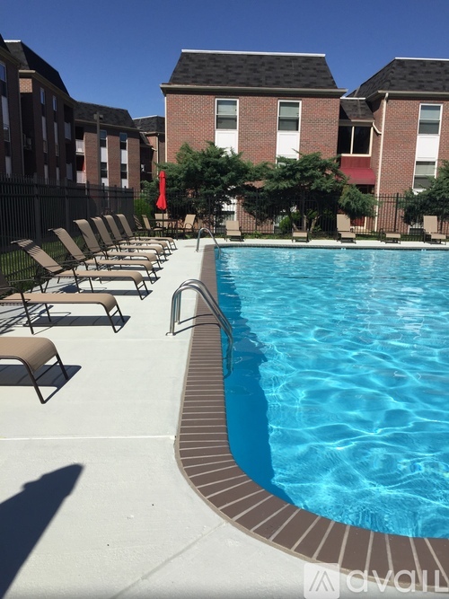 A pool with chairs around it and apartment buildings in the background.