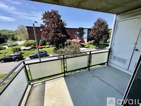 A balcony with a glass railing overlooks a parking lot and apartment buildings.