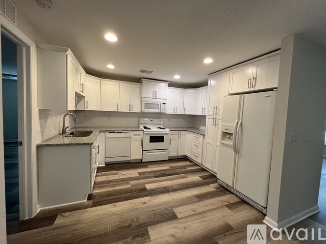 A kitchen with white cabinets and appliances on a wooden floor.
