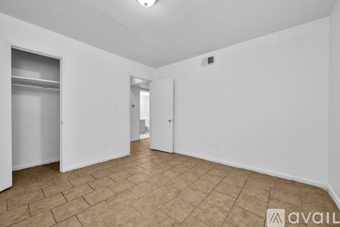 A room with tiled flooring and white walls, with a doorway leading to another room.