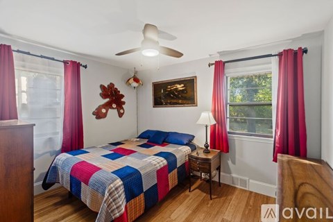 A bedroom with a bed, a fan, a table, and a painting on the wall.