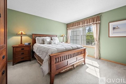 A bedroom with a large bed, a nightstand, and a window with curtains.