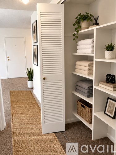 A bathroom with a white door and a white shelf with towels and a plant.