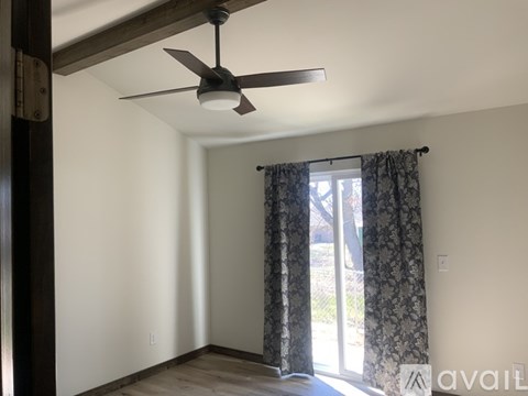 A room with a ceiling fan and a window with curtains.