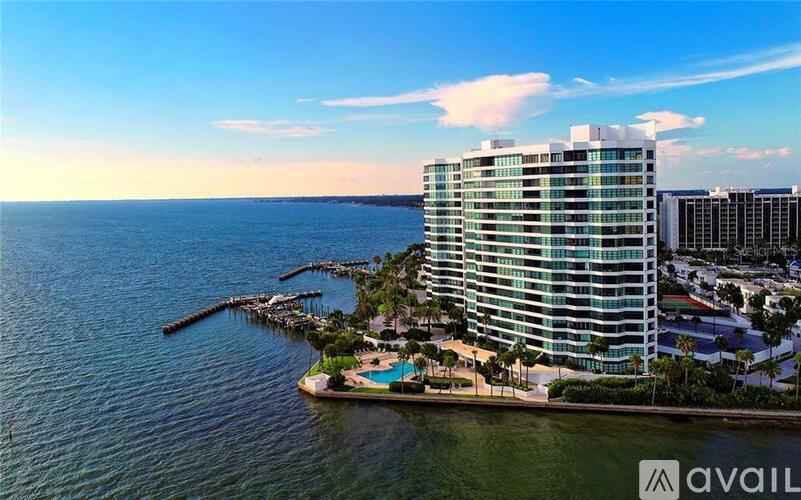 A tall building with a pool in front of it is situated on a pier by the water.