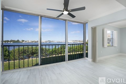 A room with a ceiling fan and sliding glass doors that opens to a balcony with a view of the beach.