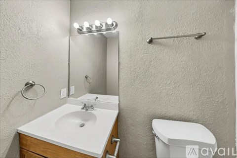 A bathroom with a white sink, toilet, and a mirror with lights above it.