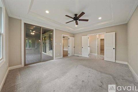 A spacious room with a ceiling fan and sliding glass doors leading to a balcony.
