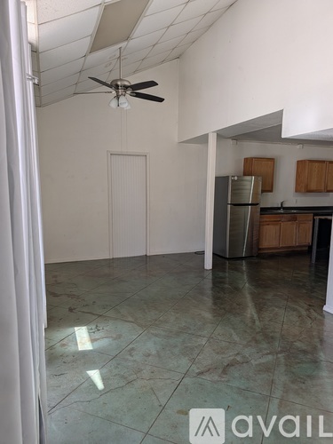 A room with a ceiling fan and a kitchen area in the background.