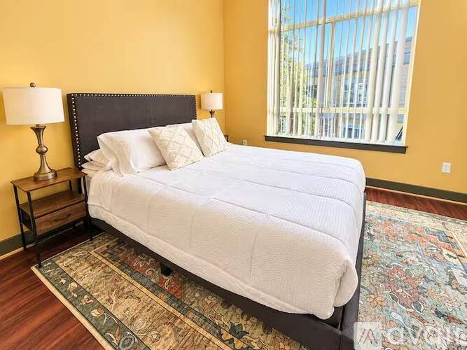 A bedroom with a large bed and a window with blinds.