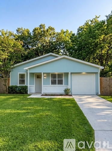 A small house with a white garage door is surrounded by a green lawn.