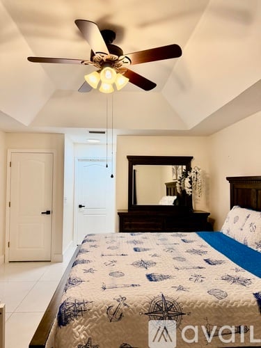 A bedroom with a bed, dresser, mirror, and ceiling fan.