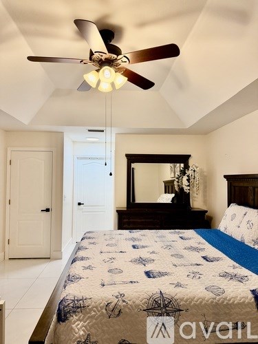 A bedroom with a bed, dresser, mirror, and ceiling fan.