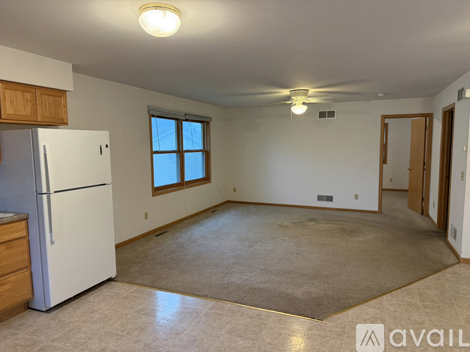 A spacious room with a refrigerator, a ceiling fan, and a window.